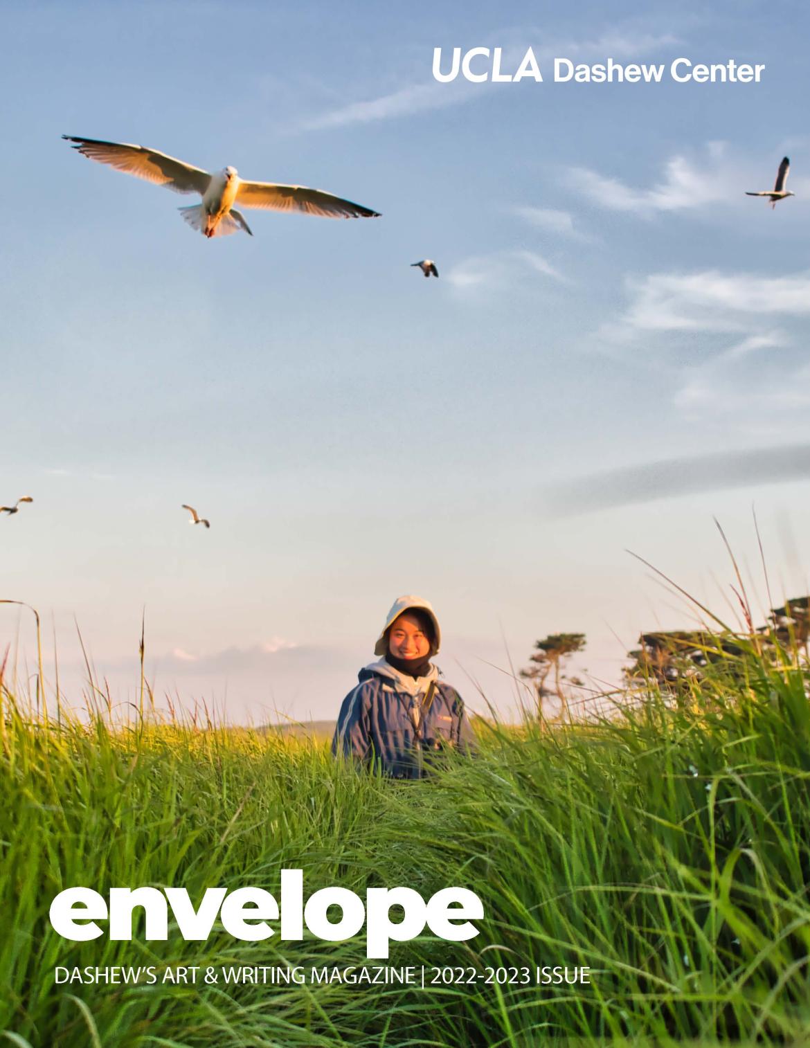 cover of Envelope Magazine featuring photo of smiling person in background with tall grass in front and birds flying overhead