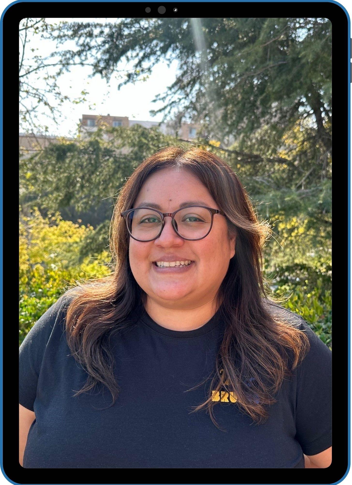 photo of assistant director, woman with brown hair against green tree filled backdrop
